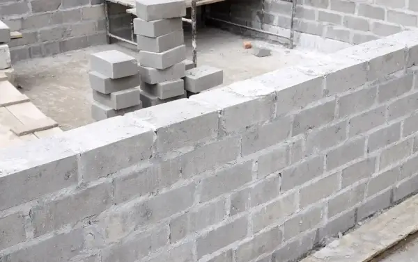 Ściana z bloczków fundamentowych w trakcie budowy. Widać stosy bloczków, gotowe fragmenty muru i zbrojenie. Bloczek fundamentowy wymiary są kluczowe dla stabilności.