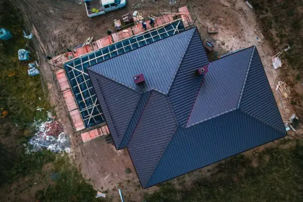 Trwa wymiana dachu na domu jednorodzinnym. Nowe pokrycie z ciemnej dachówki, widoczne kominy i rusztowania.