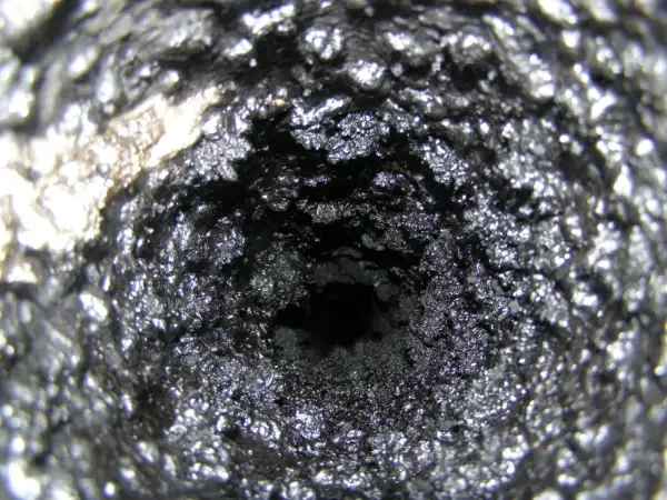Wnętrze komina pokryte grubą warstwą sadzy i kreozotu, tworzącą chropowatą, ciemną powierzchnię.
