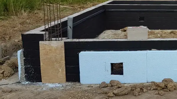 Fundamenty domu w budowie. Czarny mur z izolacją, płyta OSB i styropian. Praca murarza w toku.